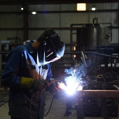 Lasser met beschermende helm aan het lassen van een metalen constructie in een werkplaats.