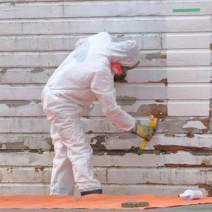 Medewerker in beschermend pak verwijdert mogelijk asbest van gevelbekleding.